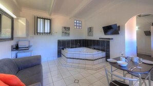 A modern bathroom with a bathtub, a sink, and a toilet. There is a flat-screen TV mounted on the wall and a window with bars. - Twin Swans Motel (Inverell)