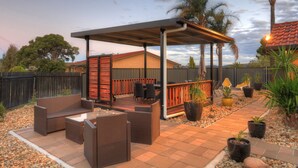 An outdoor patio area with wicker furniture, a covered seating area, and potted plants. - Twin Swans Motel (Inverell)