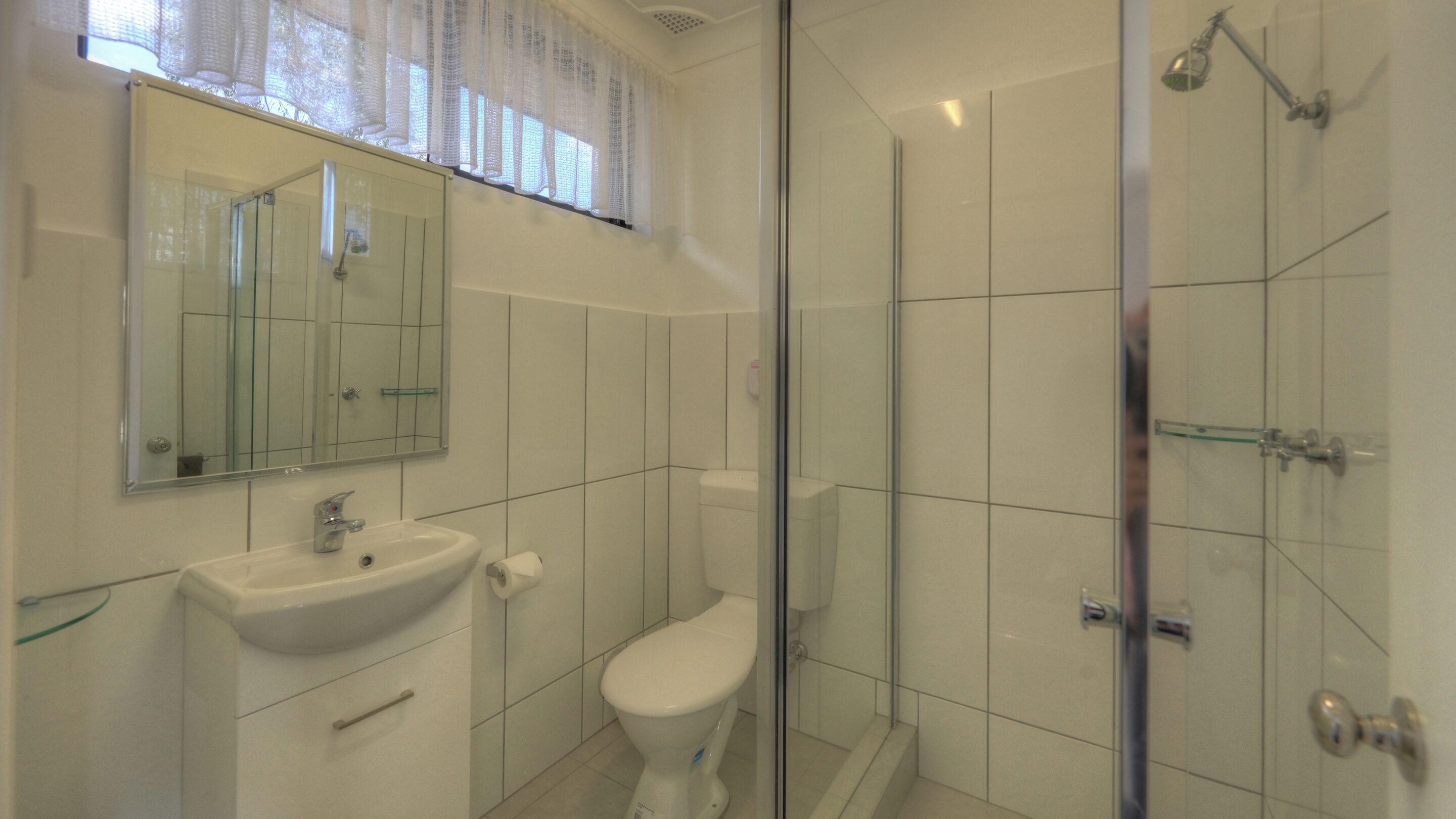 Un baño con ducha de vidrio, lavamanos e inodoro.