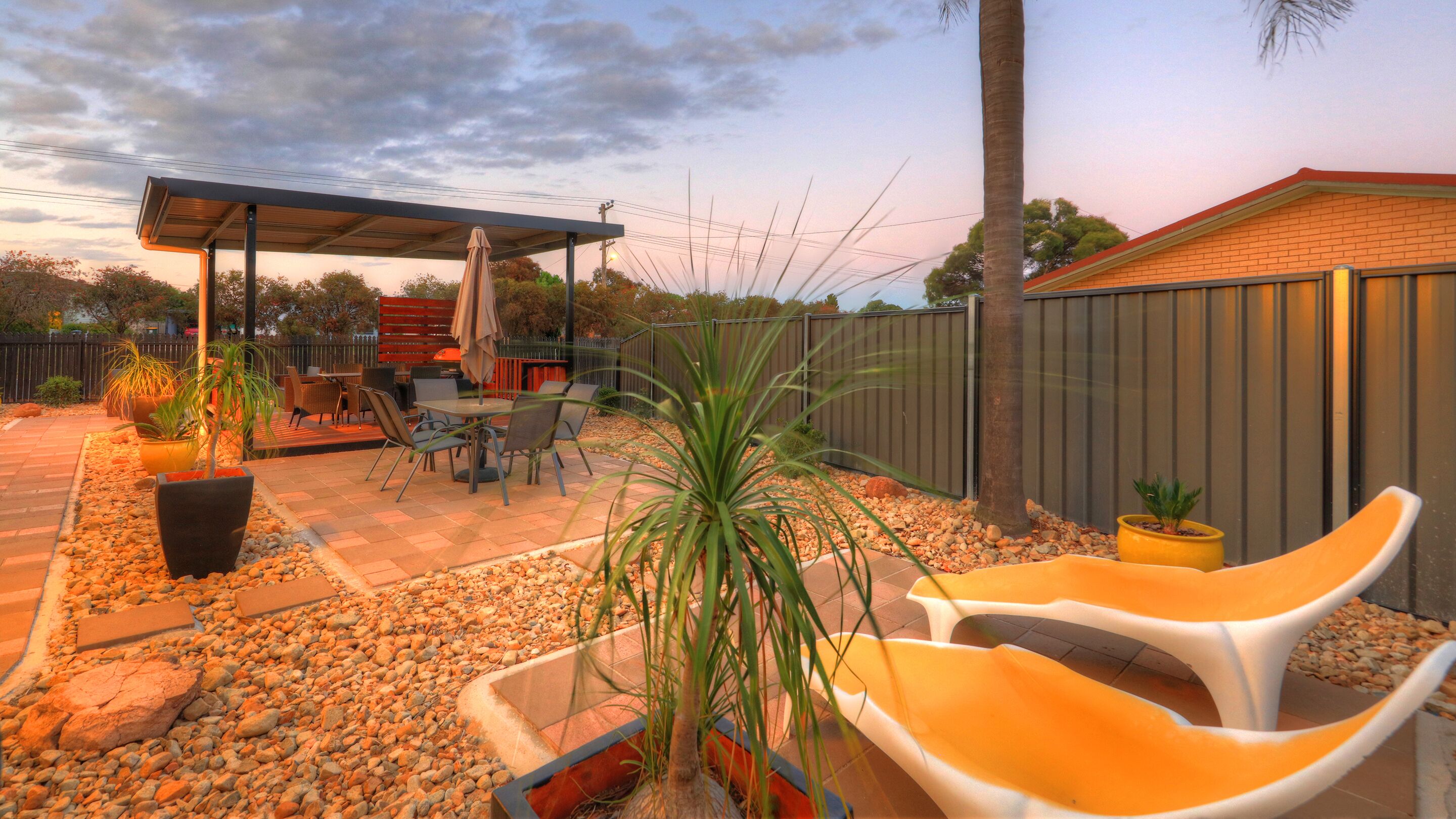 An outdoor patio area with a covered seating area, a table with chairs, and a variety of potted plants.
