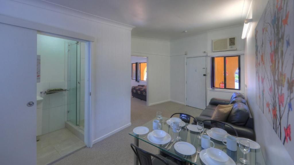 Un comedor con una mesa de vidrio preparada para cuatro personas, un sofá y una puerta que da al baño.