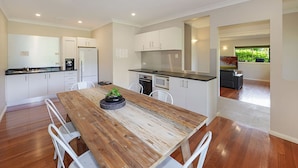 A modern kitchen with white cabinets, a wooden dining table, and a view of a garden through a window. - The Acreage Boutique Guesthouse (Picketts Valley)
