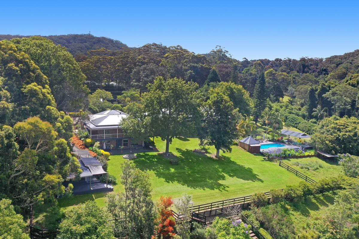 A large house with a swimming pool, surrounded by lush greenery and hills.