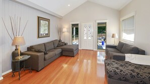 A spacious living room with a wooden floor, grey sofas, a glass coffee table, and a framed picture on the wall. - The Acreage Boutique Guesthouse (Picketts Valley)