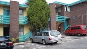 A parking lot with a building that has a brick facade and blue accents. There are two cars parked in front of the building. - Coburg Motor Inn (Coburg North)