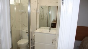 A bathroom with a glass-enclosed shower, a toilet, and a sink with a mirror above it. - Coburg Motor Inn (Coburg North)