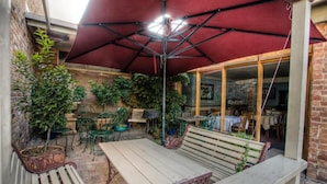 An outdoor patio area with a red umbrella, wooden benches, and potted plants. - Steampacket Inn (Echuca)