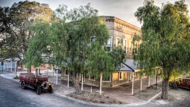 A vintage car parked in front of a building with a classical architectural style, surrounded by trees. - Steampacket Inn (Echuca)