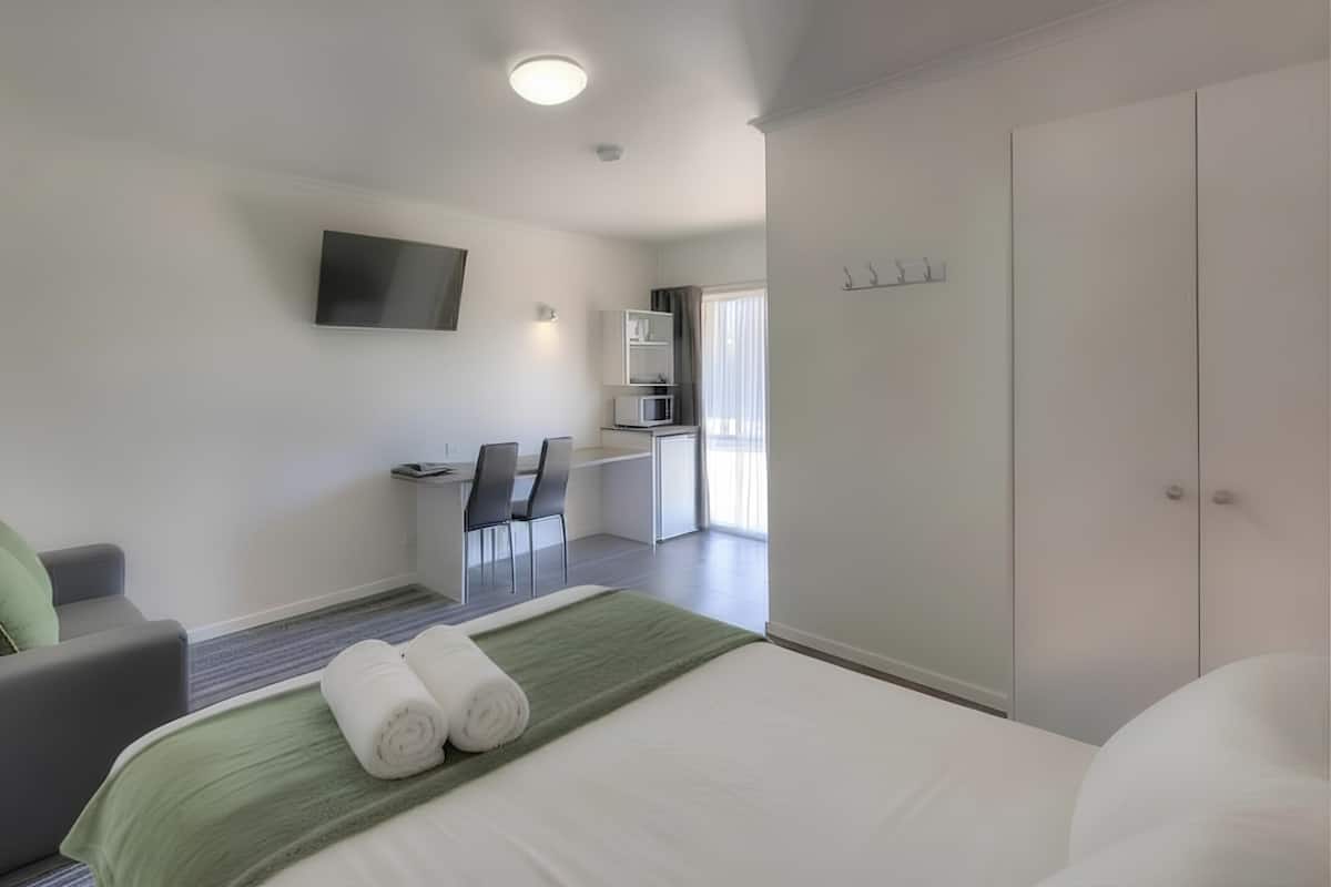Une chambre d’hôtel comprenant un lit, un canapé, un bureau avec des chaises, un téléviseur à écran plat et une armoire.