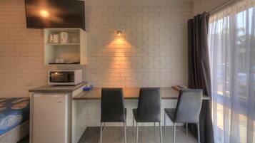 A compact kitchenette with a microwave, a small refrigerator, and a shelf with kitchenware. There are two chairs and a table in front of a brick wall.
