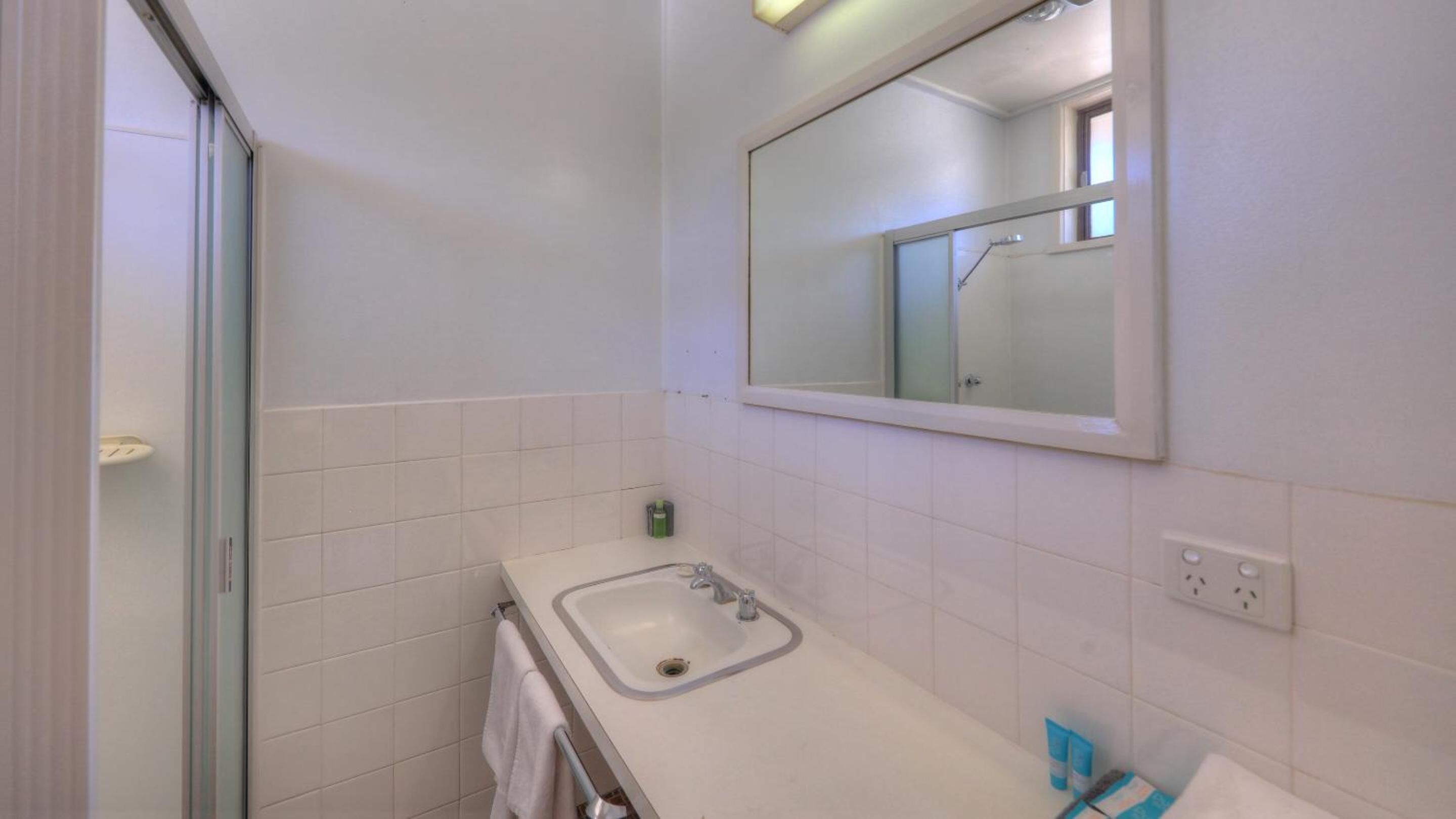 Ein Badezimmer mit einem weißen Waschbecken, einem Spiegel und einer Duschkabine.