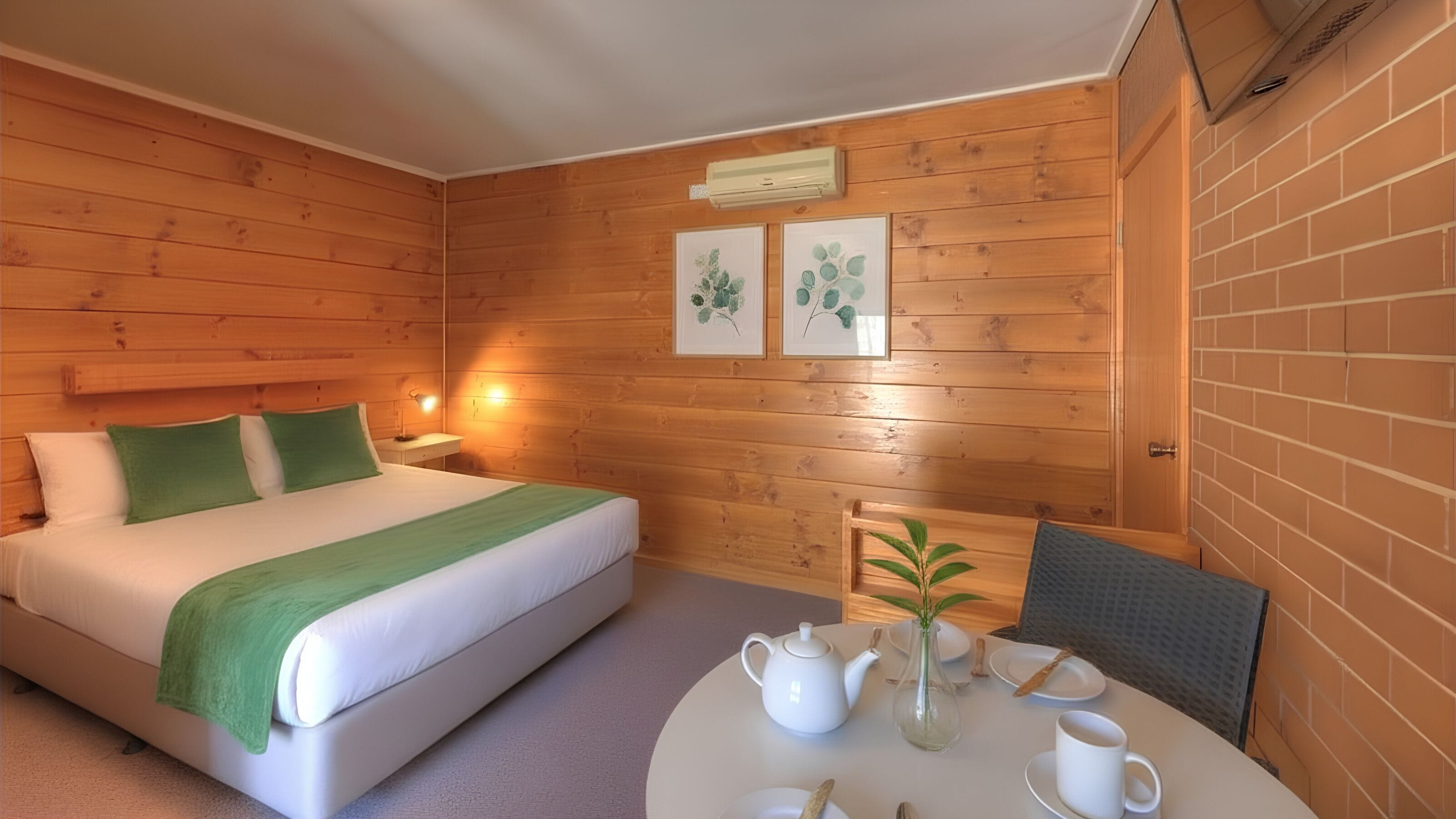 Ein Zimmer mit Holzwandverkleidung, einem Bett, einem Tisch mit Teekanne, Tassen und einer Vase, sowie zwei gerahmten Bildern an der Wand.