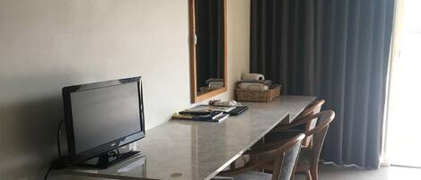 Habitación de hotel con televisión de pantalla plana, refrigerador pequeño, escritorio de madera y espejo.