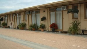 A row of motel rooms with individual air conditioning units, potted plants, and a bench outside. - Travellers Rest Motel (Bairnsdale)