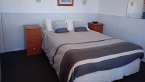 A bedroom with a bed, a dresser, a nightstand, a framed picture on the wall, and a mirror above the dresser. - Travellers Rest Motel (Bairnsdale)