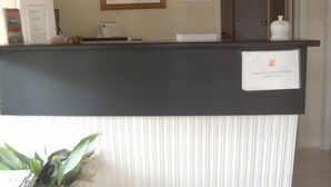 A reception desk with a framed picture above it, a sign indicating the office is closed, and a potted plant to the left. - Travellers Rest Motel (Bairnsdale)