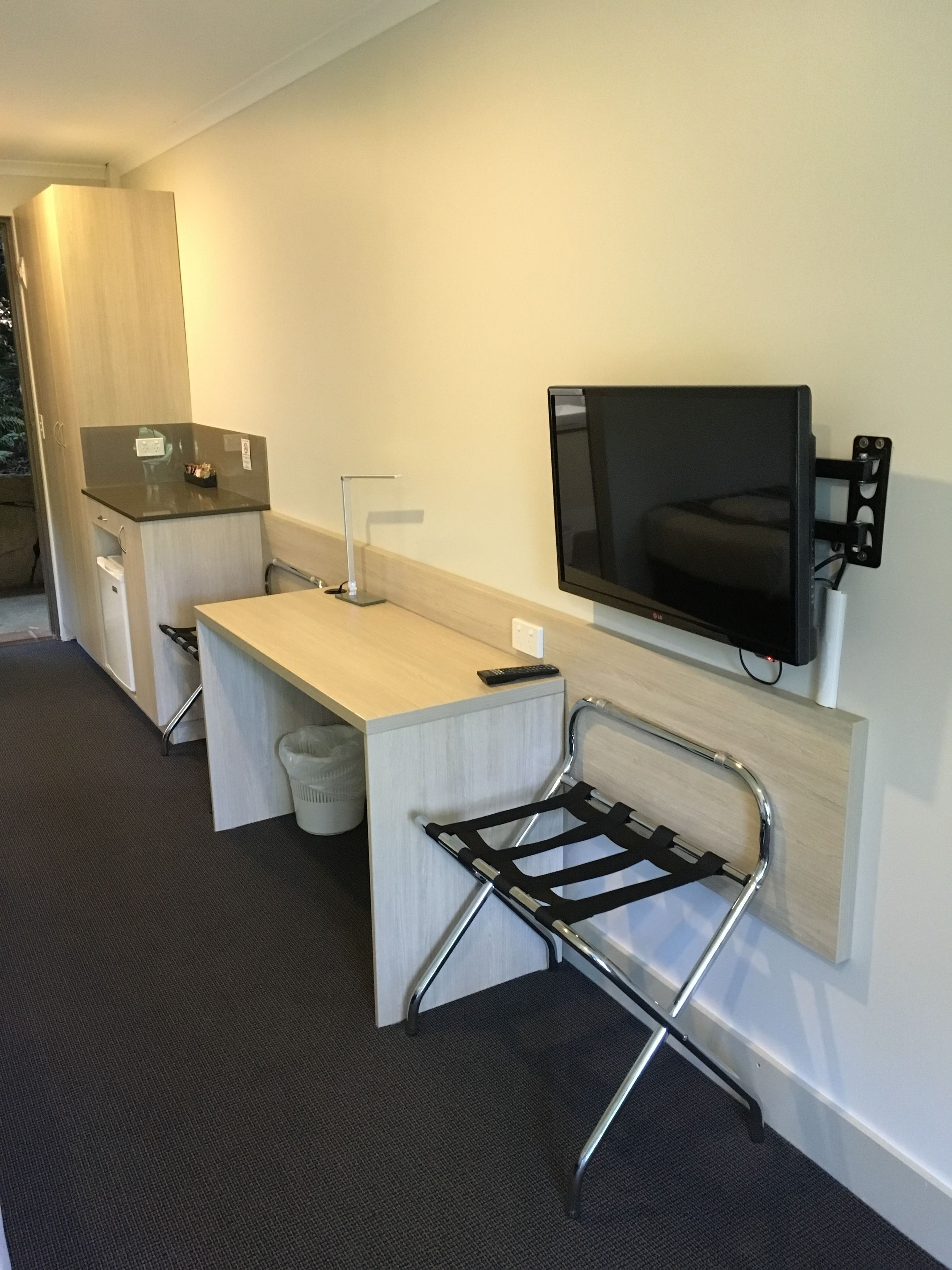 Una habitación de hotel compacta con kitchenette, un televisor de pantalla plana montado en la pared y una silla plegable.