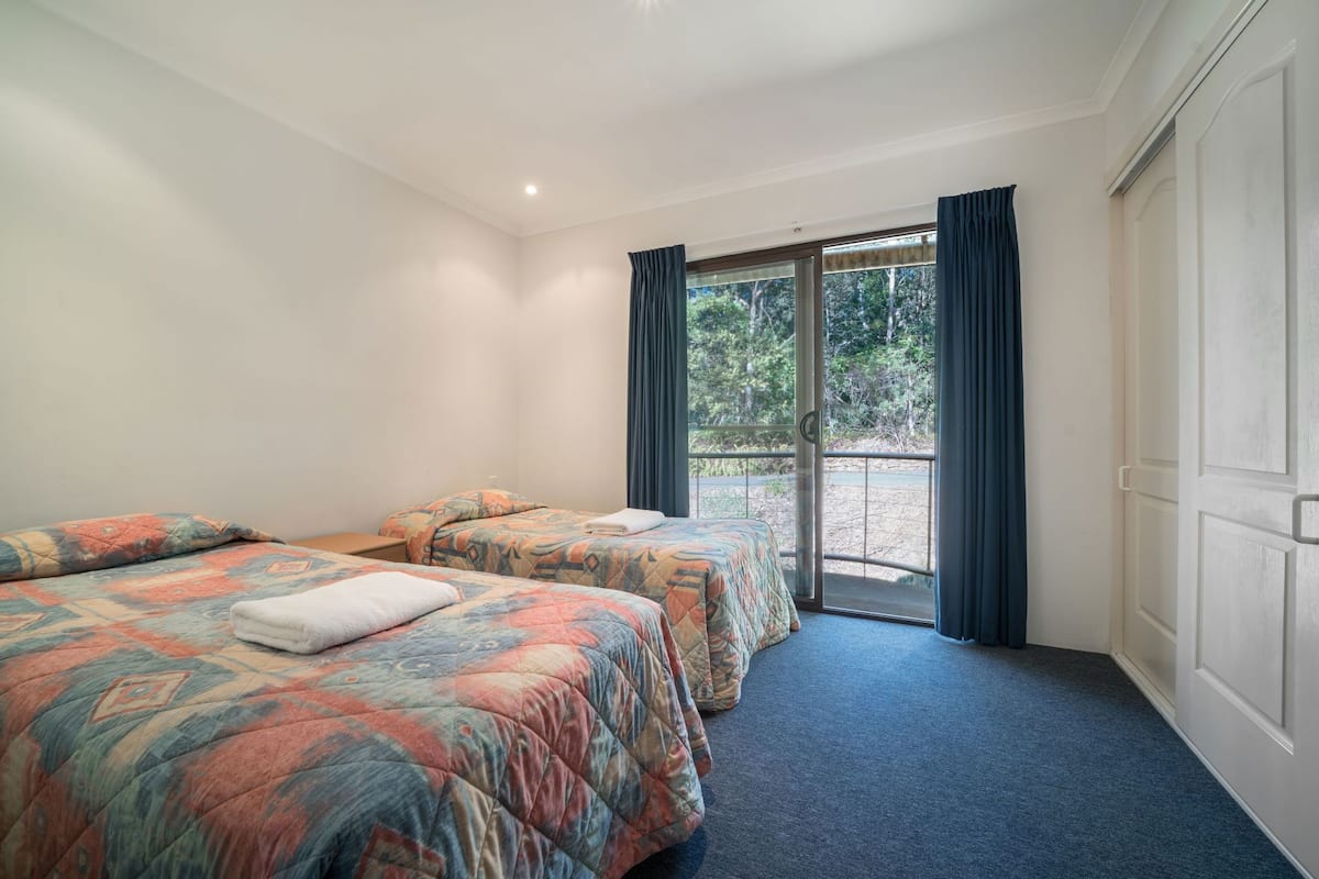 A hotel room with two beds, a large sliding glass door leading to an outdoor area, and a wardrobe.