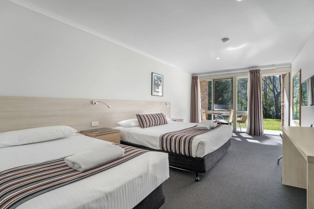 A hotel room with two beds, a desk, and a view of the outdoors.
