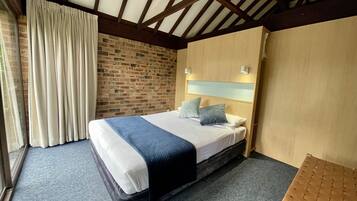 Un dormitorio con cama, pared de ladrillo, techo de madera y ventana con cortinas.