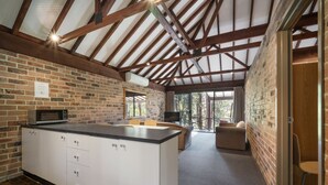 A modern kitchen with a large island, wooden beams, brick walls, and a cozy seating area with a TV. - Avoca Beach Hotel (Avoca Beach)