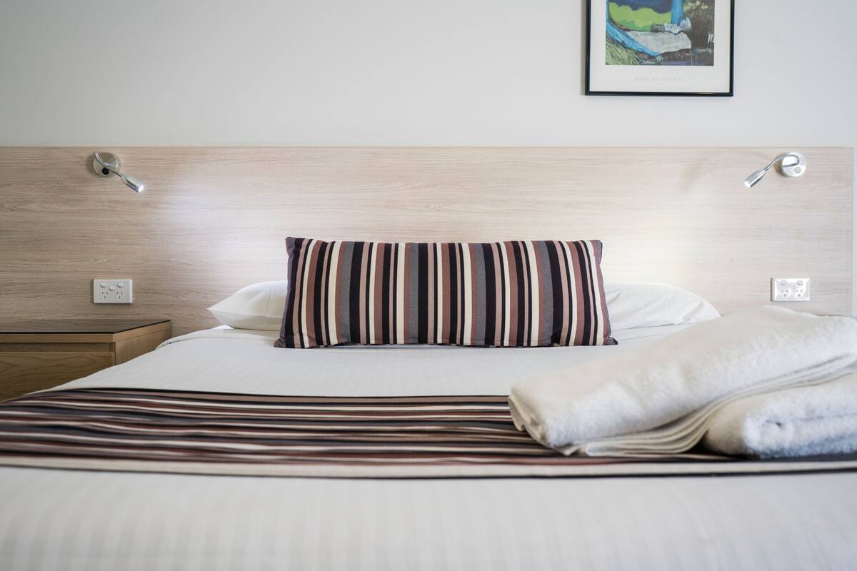A neatly made bed with striped bedding, a pillow, and a folded blanket.