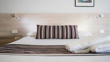 A neatly made bed with striped bedding, a pillow, and a folded blanket.