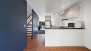 A modern kitchen with white cabinets, a central island, and a staircase leading to another level. - Avoca Beach Hotel (Avoca Beach)