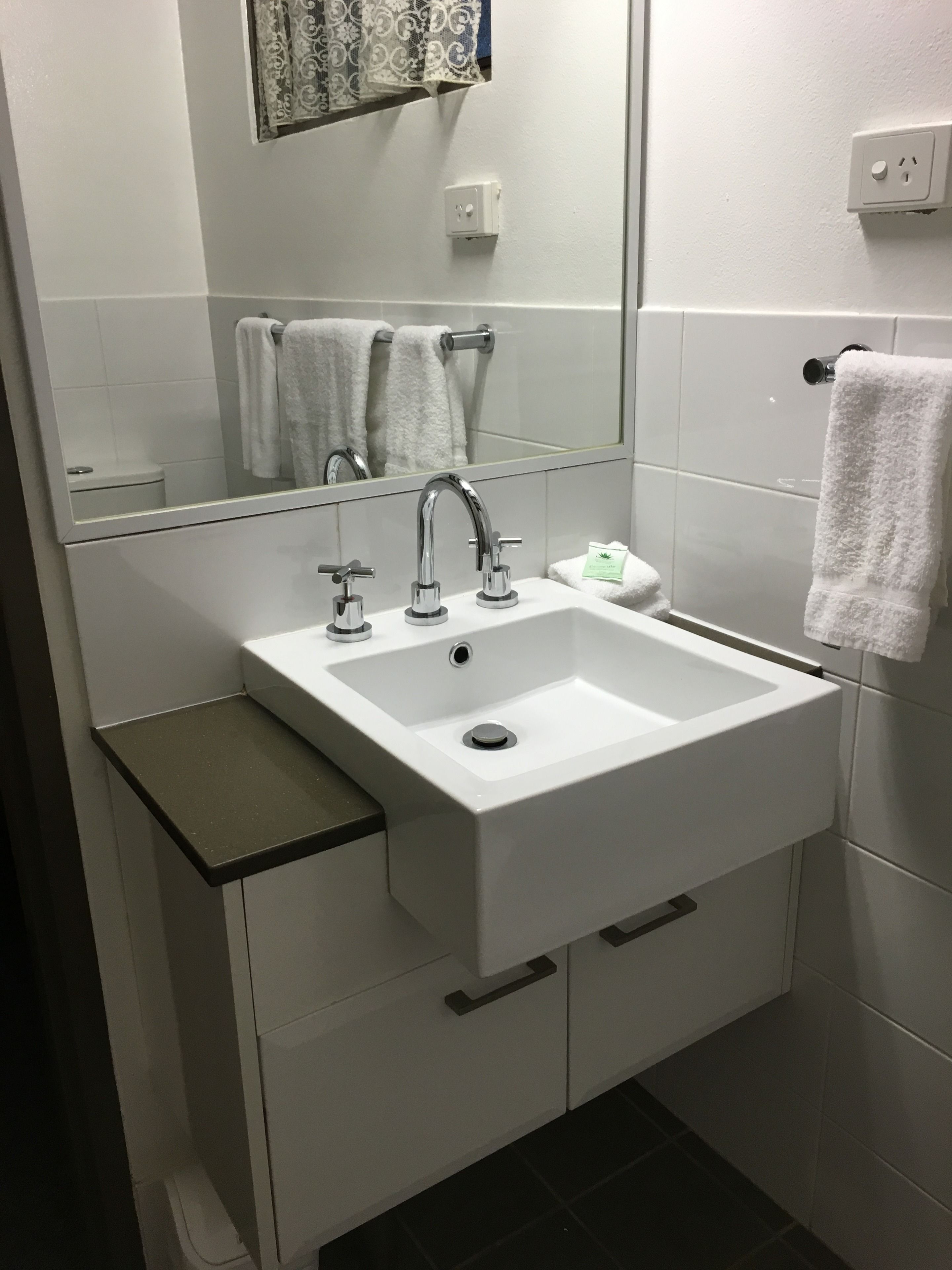 A modern bathroom with a white sink, two faucets, a mirror, and a towel rack.