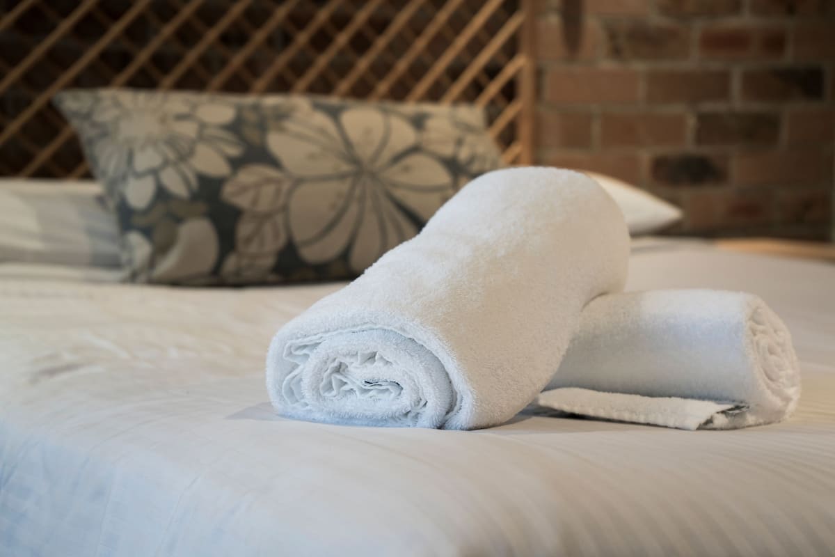A neatly made bed with a rolled white towel and a floral pillow.
