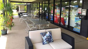 Un patio al aire libre con mesas y sillas, un sofá con un cojín y un muro de cristal con anuncios.