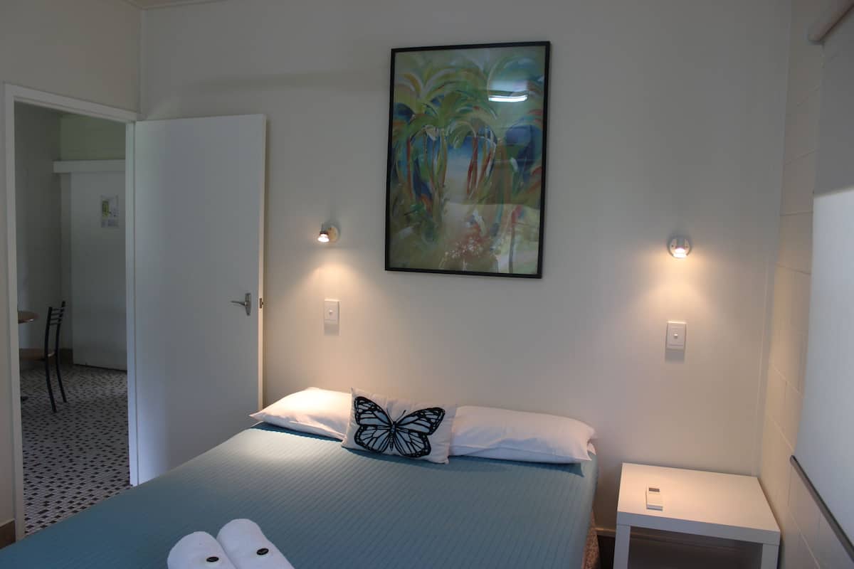 A bedroom with a bed, a pillow with a butterfly design, a nightstand, and a wall-mounted painting.