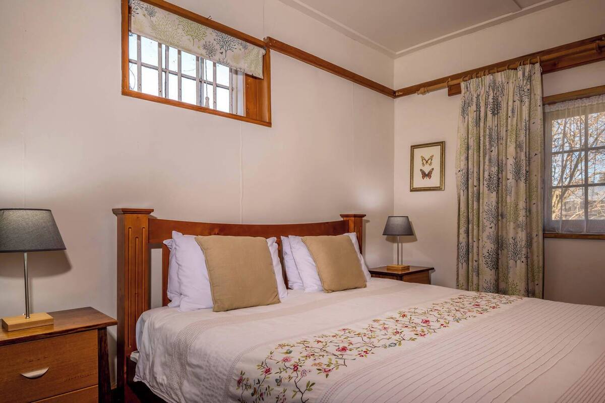 A bedroom with a wooden bed, two bedside tables, a window with curtains, and a wall-mounted picture.