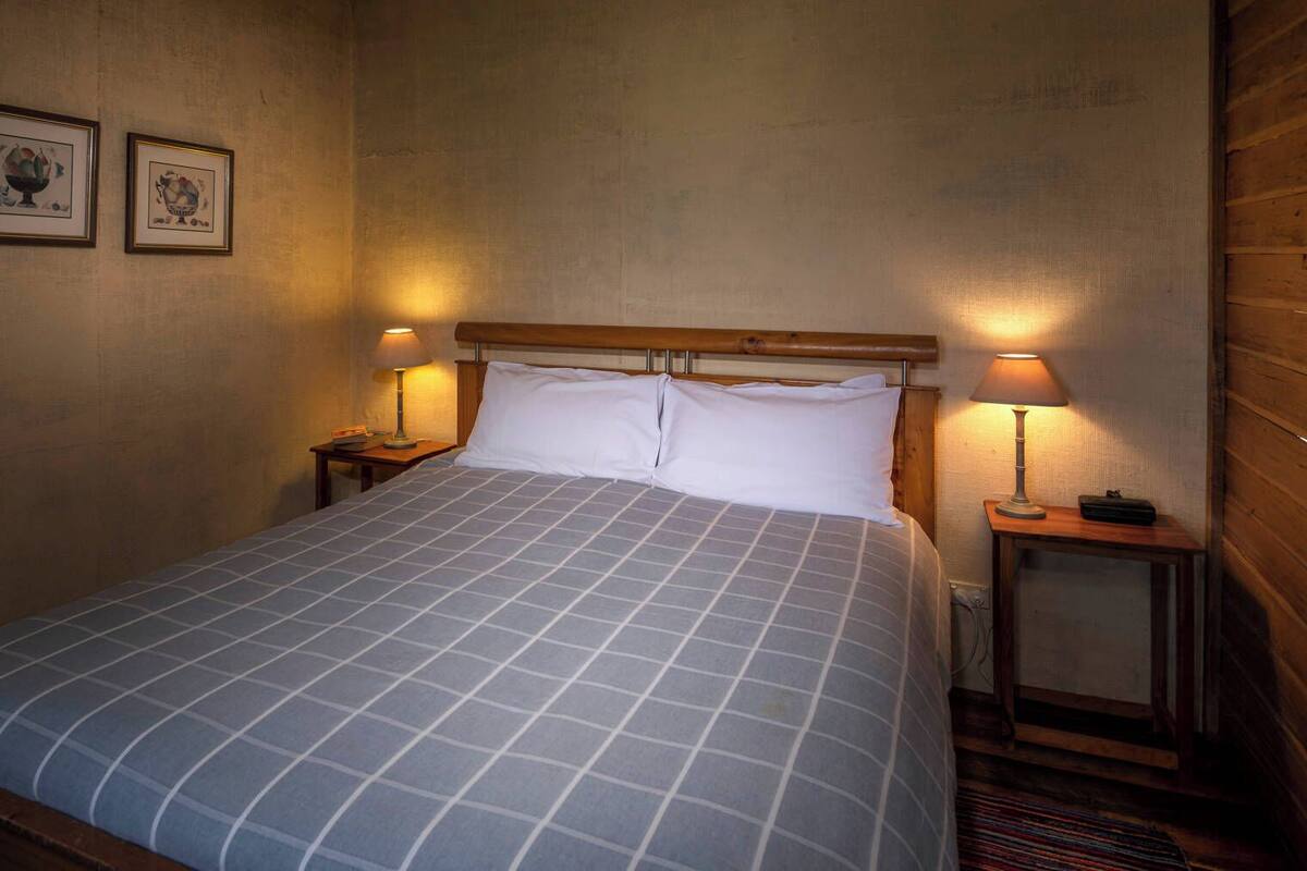 A neatly made bed with a checkered bedspread, two bedside lamps, and two framed pictures on the wall.