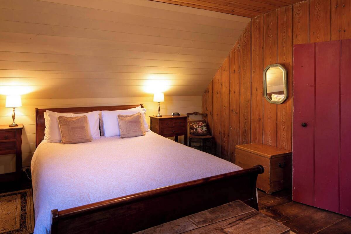 A cozy bedroom with a wooden bed, two bedside tables with lamps, a nightstand, a dresser, and a mirror on the wall.