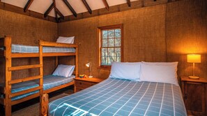 A room with bunk beds, a single bed, a window with a view, a bedside table with a lamp, and a nightstand.