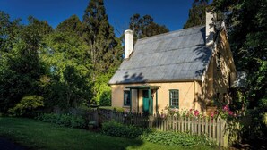 Una casa senyorial amb teulada inclinada, envoltada de vegetació abundant i una tanca de fusta.