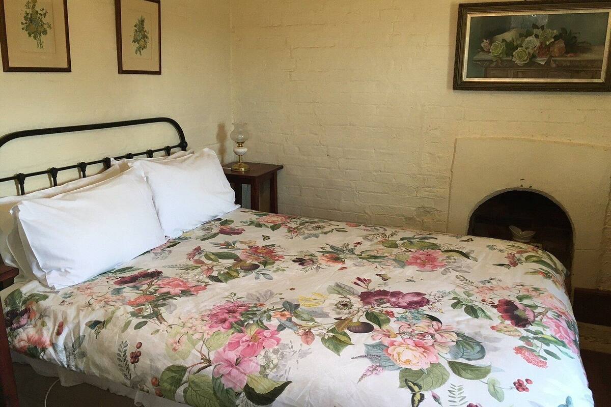 A bedroom with a floral bedspread, a metal bed frame, a bedside table with a lamp, and a fireplace.