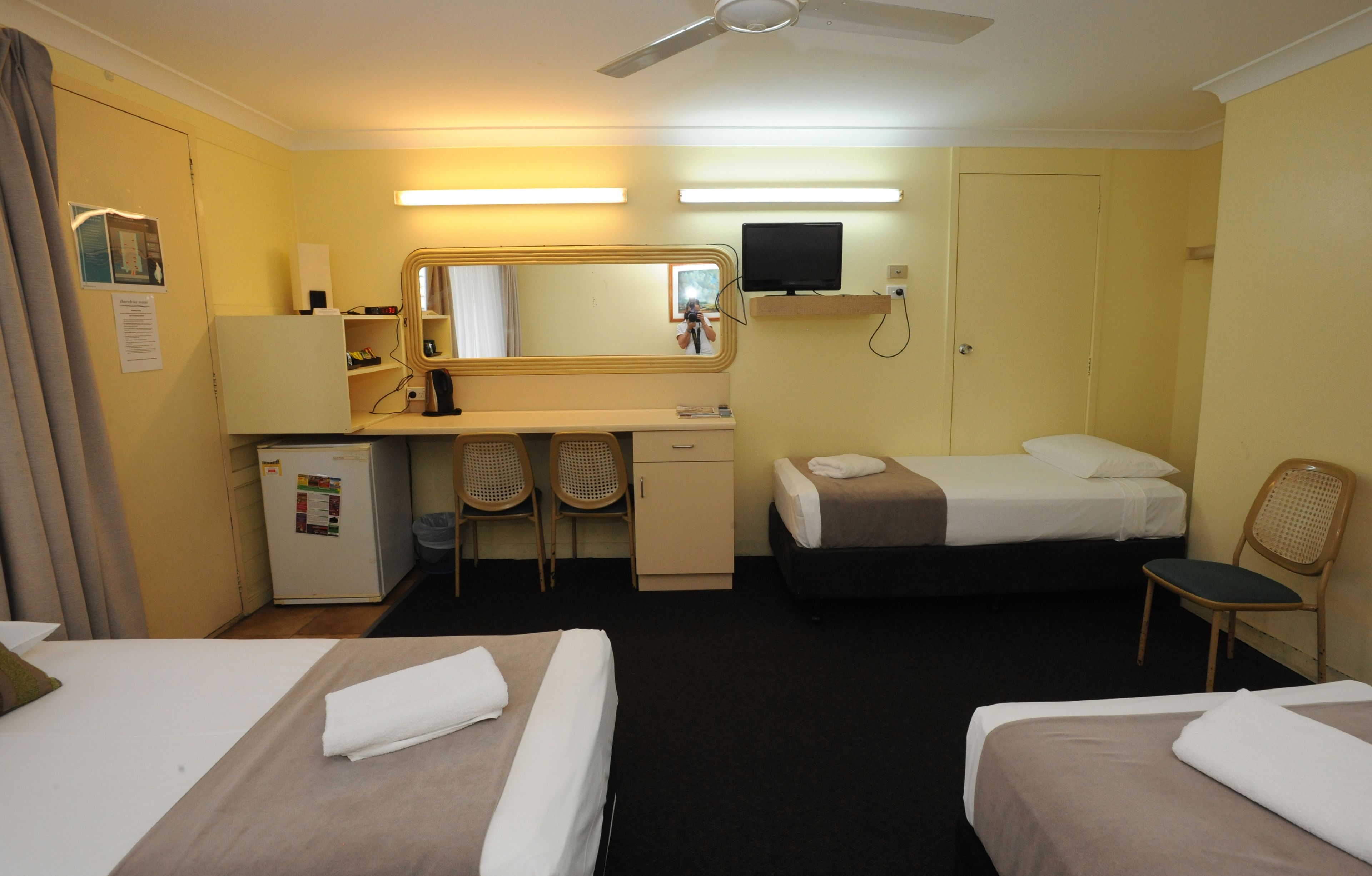 A hotel room with two beds, a desk, a chair, a television, and a ceiling fan.