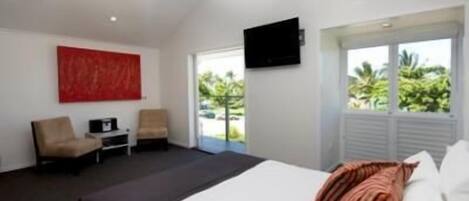 Una habitación de hotel moderna con una cama grande, un ventilador de techo, un televisor montado en la pared y vistas al exterior a través de un amplio ventanal.