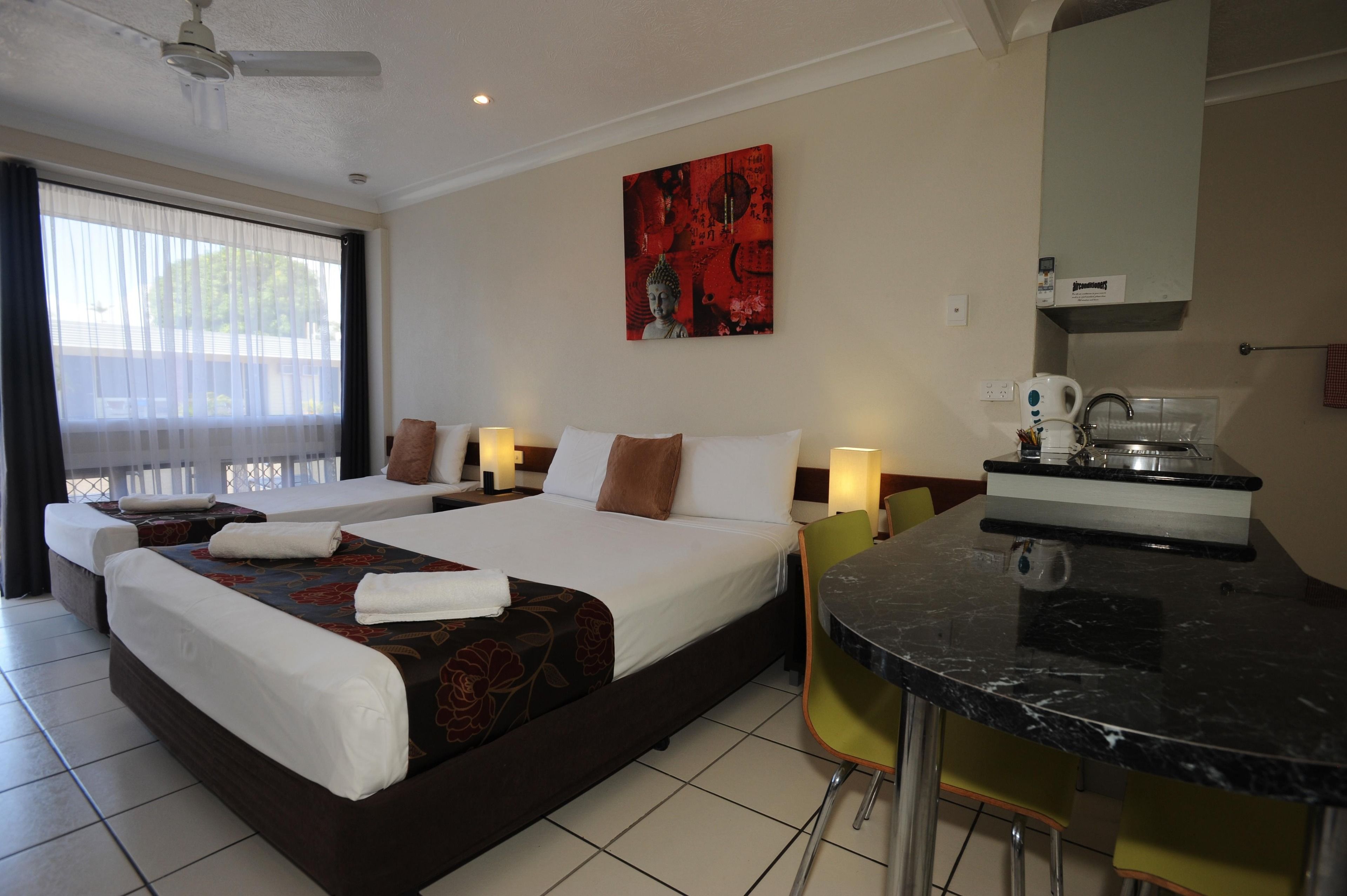 A hotel room with a large bed, a desk with a chair, a window with curtains, and a painting on the wall.