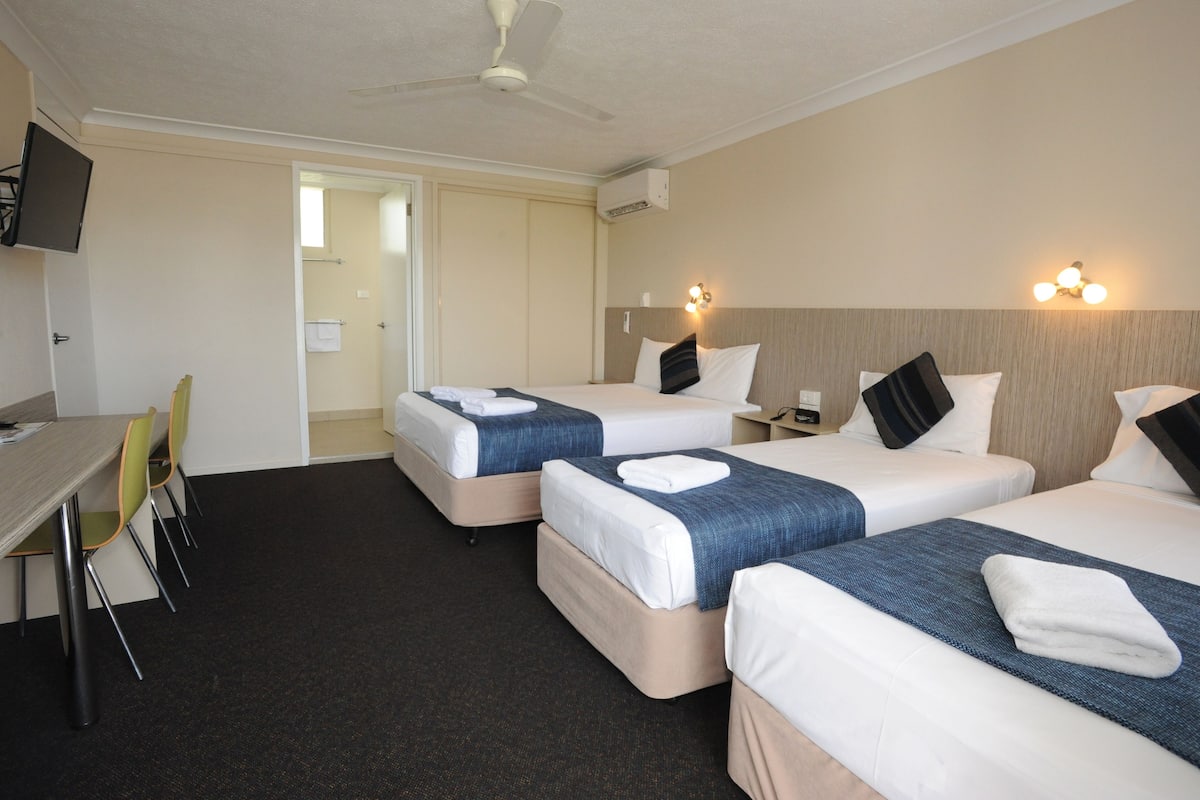 A hotel room with two beds, a desk, chairs, and a TV.