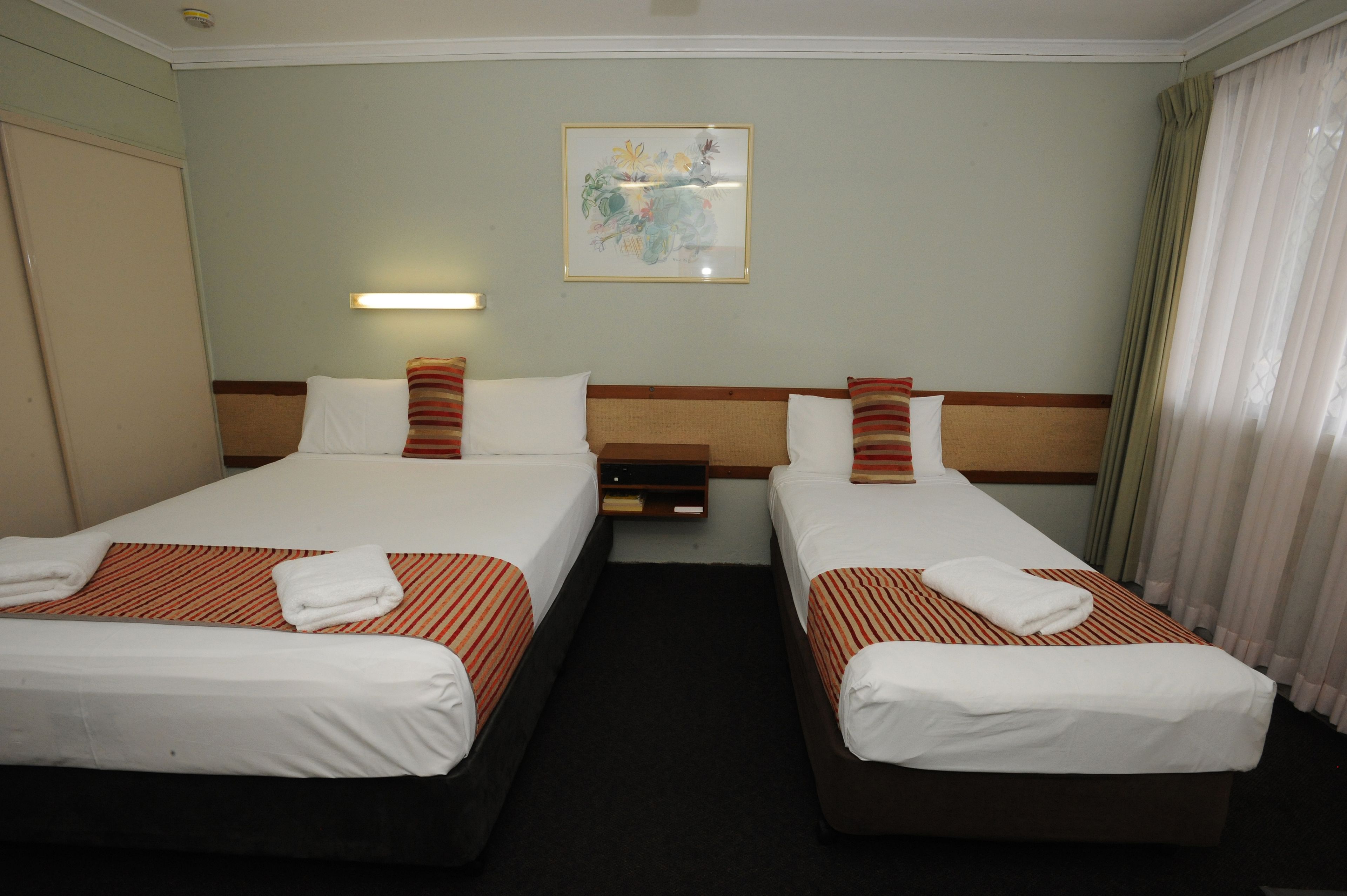 Una habitación de hotel con dos camas, una mesita de noche, una lámpara de pared y un cuadro.