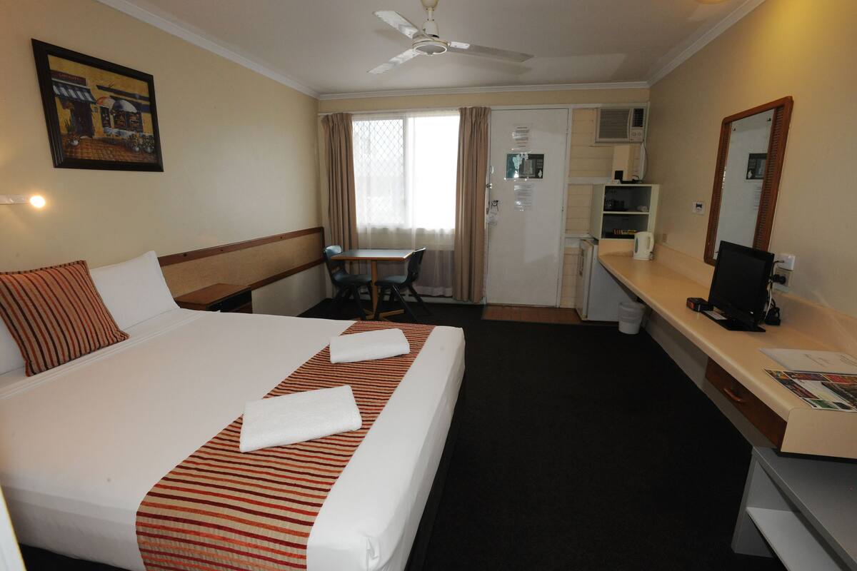 A hotel room with a large bed, a desk, a chair, a small table, a mirror, and a ceiling fan.