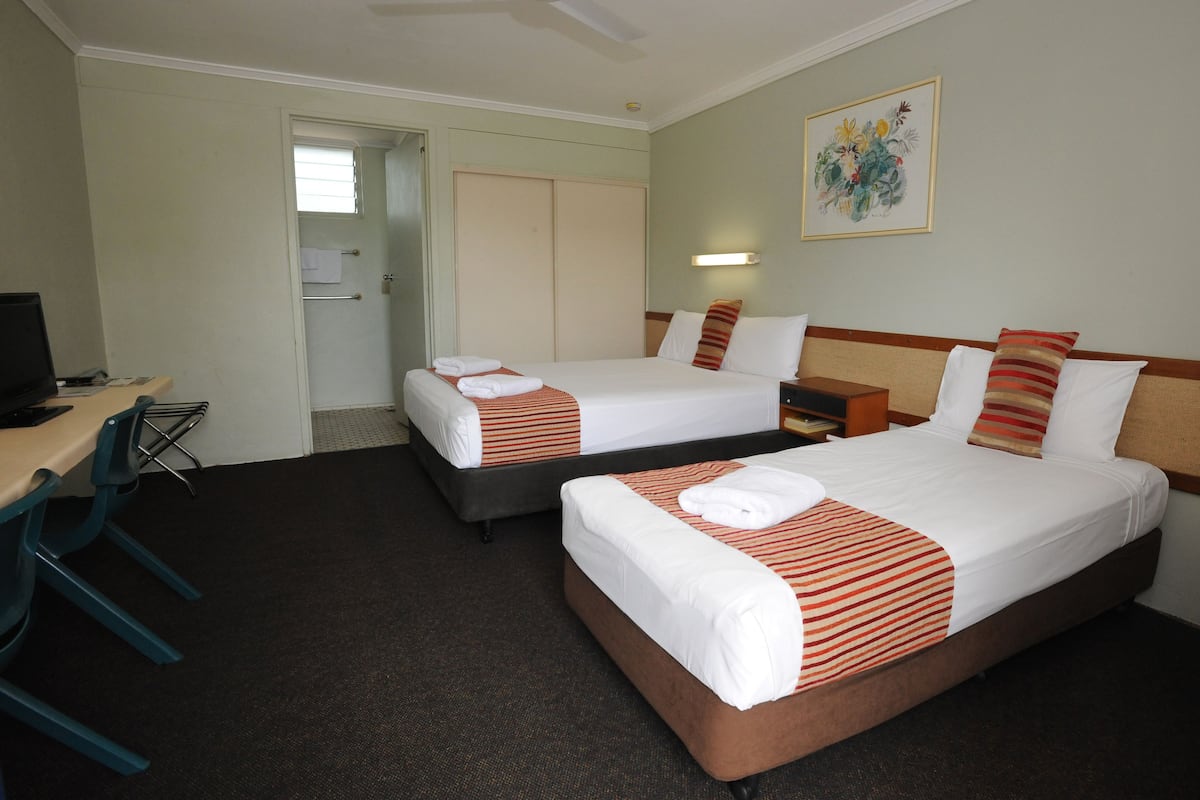 A hotel room with two beds, a desk, a chair, a TV, and a painting on the wall.
