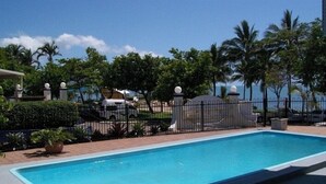 Una piscina con valla y palmeras al fondo.