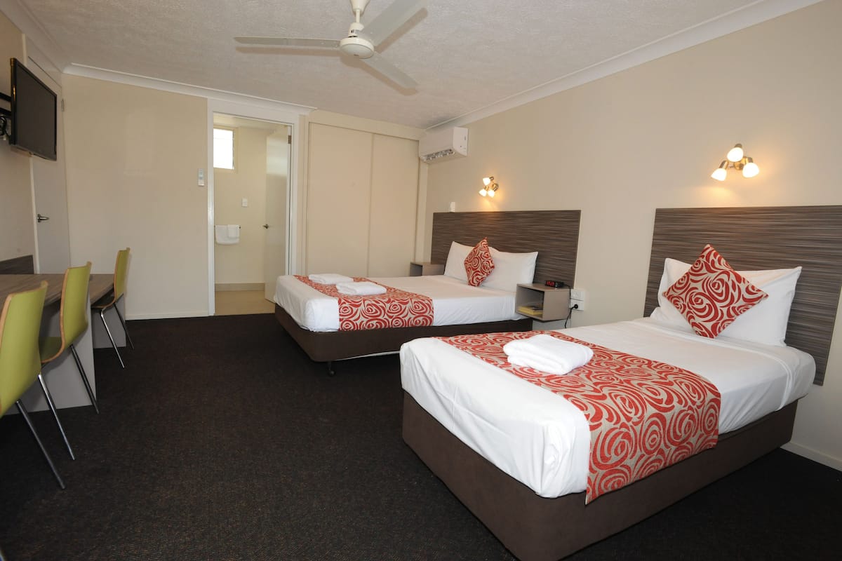 A hotel room with two beds, a dining area with chairs, a ceiling fan, and a TV.