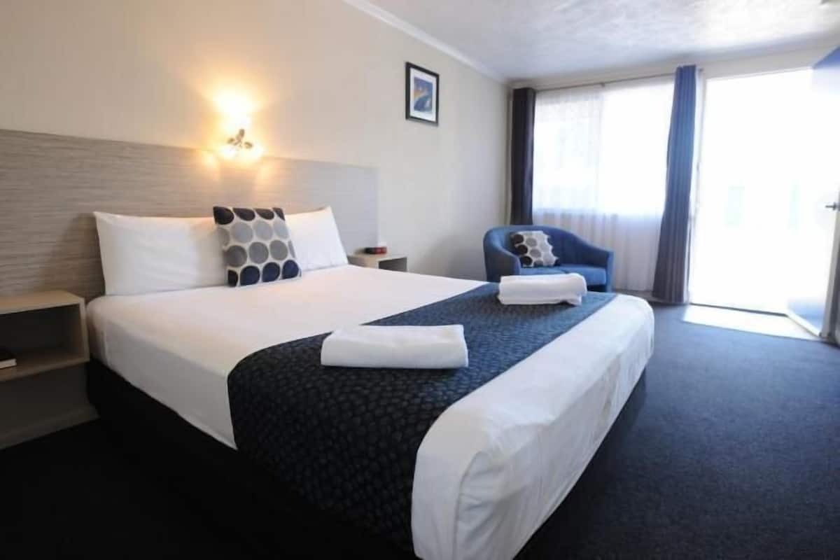 A hotel room with a large bed, a bedside table, a chair, and a window with curtains.