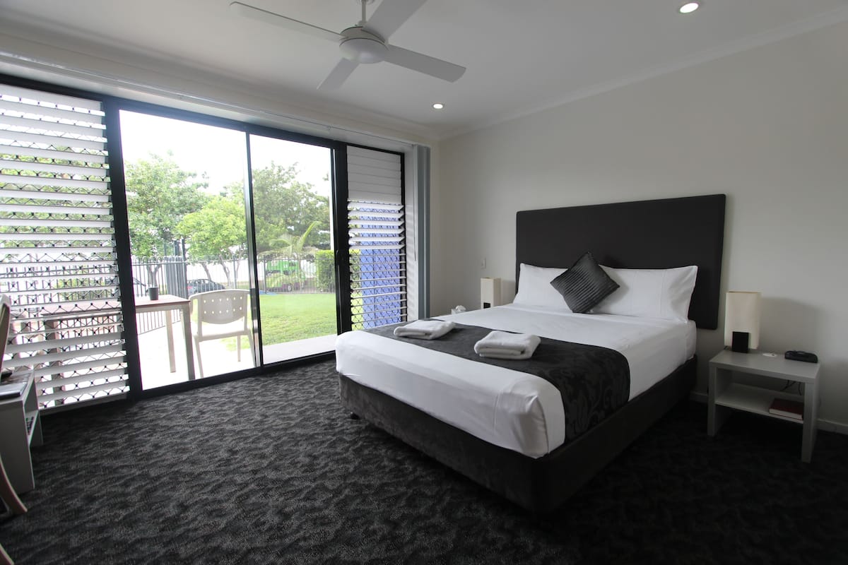 A hotel room with a large bed, a ceiling fan, a desk, and a view of the outdoors through a sliding glass door.