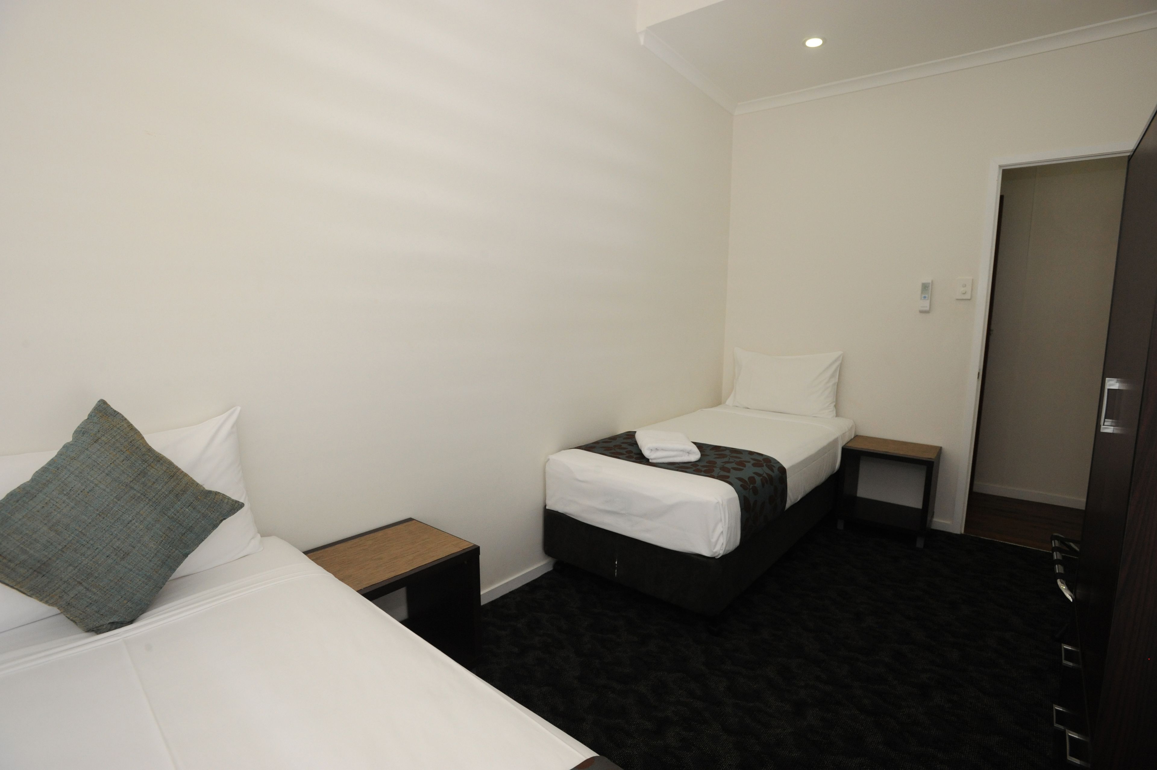 A small, clean room with two beds, a bedside table, and a door.
